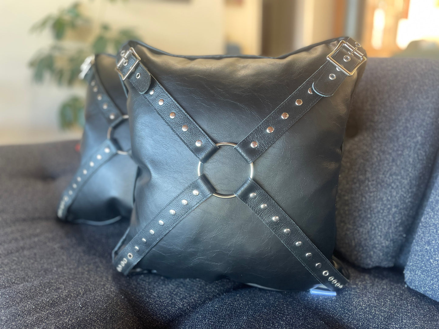 Photo of two black leather pillows with black harnesses on them.