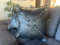 Photo of two black leather pillows with black harnesses on them.